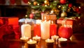 Closeup image of lots of burning candles and gifts against glowing Christmas tree at living room