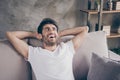 Closeup photo of mixed race guy sitting cozy sofa holding hands behind head relaxing homey weekend mood looking dreamy