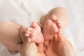 Closeup photo of mother`s hands holding baby`s small feet on isolated white cloth background Royalty Free Stock Photo