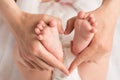 Closeup photo of mother`s hands holding newborn`s small feet and making heart with fingers on isolated white cloth background Royalty Free Stock Photo