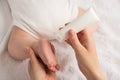 Closeup photo of newborn laying on stomach and mother`s hands holding baby`s leg and white lotion tube on isolated white blanket Royalty Free Stock Photo