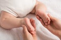 Closeup photo of newborn laying on stomach and mother`s hands holding small feet on isolated white cloth background Royalty Free Stock Photo