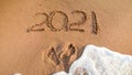 Closeup image of 2021 numbers written on sand and footprints on sea beach. Concept of New Year, Christmas and travel on Royalty Free Stock Photo