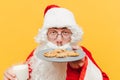 Closeup photo of Santa Claus smelling the tasty chocolate cookies, holding a glass of milk, feeling delighted, standing on an