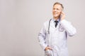 Closeup photo of senior man doctor standing isolated on grey background, using mobile phone Royalty Free Stock Photo