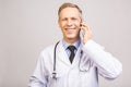 Closeup photo of senior man doctor standing isolated on grey background, using mobile phone Royalty Free Stock Photo