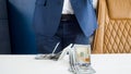 Closeup image of stack of money lying on office desk in front of businessman in blue suit