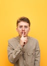 Closeup photo of surprised young man in glasses and mustache on yellow background, shows silence sign and with shocked face looks Royalty Free Stock Photo