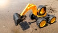 Closeup photo of toy excavator digging wet sand at beach. Concept of building and construction. Royalty Free Stock Photo