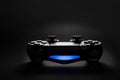 Closeup photo of video game console gamepad joystick controller on black background with blue light.