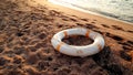 Closeup image of white plastic life saving ring lying on the sandy sea beach against beutiful sunset over the water Royalty Free Stock Photo