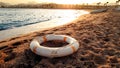 Closeup image of white plastic life saving ring lying on the sandy sea beach against beutiful sunset over the water Royalty Free Stock Photo