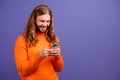 Closeup photo of young cheerful blond hair guy wearing orange sweater texting his friends hipsters isolated over purple Royalty Free Stock Photo