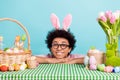 Closeup photo of young funny hairdo chevelure guy wear bunny ears easter folded arms desk fresh flower painted eggs