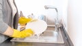 Closeup image of young housewife in gloves washing off suds from dishes Royalty Free Stock Photo