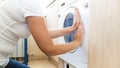 Closeup photo of young woman closing dorr of washing machine full of dirty clothes