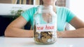 Closeup photo of young woman sitting behind desk with glass jar full of money for purchasing new house Royalty Free Stock Photo