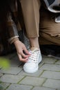 Closeup photo of young woman wearing checkered long coat, and beige pants . Lady posing on city street. Women ties laces