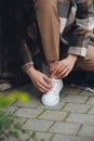 Closeup photo of young woman wearing checkered long coat, and beige pants . Lady posing on city street. Women ties laces