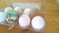 A closeup photograph of a single painted plastic Easter egg nested inside of a plastic egg carton with several real chicken eggs Royalty Free Stock Photo