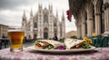 closeup of piadina with ham and cheese and a beer on the table with the background of milan cathedral blurred