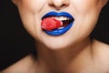 Closeup picture of cheerful girl`s colorful lips holding sweeties with teeth. Royalty Free Stock Photo
