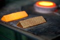 Closeup picture of ingots of melt gold, hot shiny metal bars on table and fire furnace on background