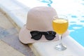 Closeup of pink straw hat and black protective sunglasses, goggles, fresh orange juice smoothie drink cocktail on hotel swimming Royalty Free Stock Photo