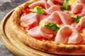 Closeup of pizza with melted mozzarella, ham, quail eggs, tomatoes and fresh greens on wooden board Royalty Free Stock Photo