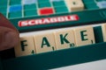 Closeup of plastic letters with word Fake in hand on Scrabble board game