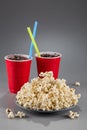Closeup popcorn on the background of red plastic cups with fizzy drink with colored straws Royalty Free Stock Photo