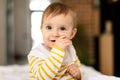 Closeup portrait of adorable baby girl sucking finger and smiling, looking at camera, sitting on bed at home interior Royalty Free Stock Photo