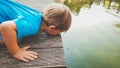 Closeup toned portrait of adorable toddler boy kneeling at river and looking at water strider floating on lake surface Royalty Free Stock Photo