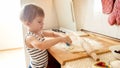 Closeup portrait of adorable 3 years old toddler boy rolling wheat dough with rolling pin and cutting cookies with