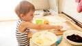 Closeup portrait of adorable 3 years old toddler boy rolling wheat dough with rolling pin and cutting cookies with