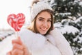 Closeup portrait amazing joyful smiling girl in sunny winter morning with pink lollypop on street. Attractive young