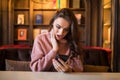 Closeup portrait anxious young girl looking at phone seeing bad news or photos with disgusting emotion on her face cafe background