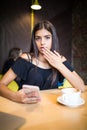 Closeup portrait anxious young girl looking at phone seeing bad news or photos with disgusting emotion on her face isolated cafe b