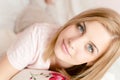 Closeup portrait of attractive beautiful young blond woman with blue eyes and excellent skin in bed & looking at camera