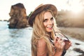 Closeup portrait of attractive blonde girl with long hair posing on rocky beach. She wears bikini, hat. She holds Royalty Free Stock Photo