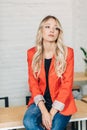 Blonde woman in red jacket smiling at camera with colleagues in background Royalty Free Stock Photo