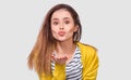 Closeup portrait of a beautful young woman wearing striped shirt and yellow jacket, sending air kiss to his boyfriend while