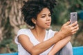 Closeup portrait of beautiful african american woman sitting outdoors in the park taking selfie and messaging via social networks Royalty Free Stock Photo