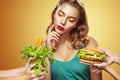 Closeup portrait. Beautiful blond young woman choosing between burger and vegetarian food. Royalty Free Stock Photo