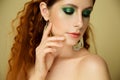 Closeup portrait of beautiful fashion model over beige background, pretty redhead woman with stylish green makeup and body art Royalty Free Stock Photo