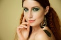 Closeup portrait of beautiful fashion model over beige background, pretty redhead woman with stylish green makeup and body art Royalty Free Stock Photo