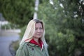 Closeup portrait of a beautiful forty-year-old blonde caucasian woman in a casual green jacket posing outdoors in a park against