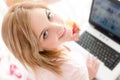 Closeup portrait of beautiful gentle sweet young woman blue eyes girl in bed with laptop and apple looking up