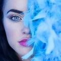 Closeup portrait of beautiful seductive brunette woman looking into the camera while playing with blue feather boa Royalty Free Stock Photo