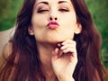 Closeup portrait of beautiful sexy woman with red lips giving kiss sign lying on green grass outdoors